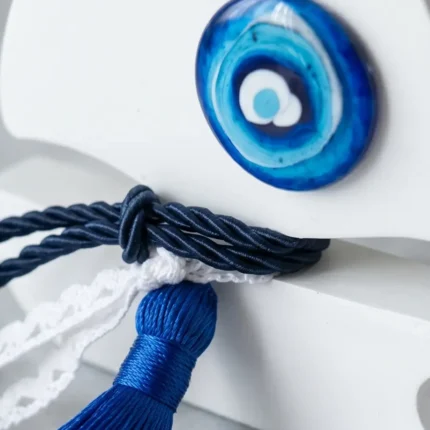 Μάκρο φωτογραφία που δείχνει το γυάλινο μπλε ματάκι, το navy κορδόνι και τη λευκή δαντέλα πάνω στην πορσελάνη.