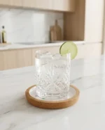 ρυστάλλινο ποτήρι με παγωμένο νερό και φέτα lime, τοποθετημένο πάνω σε αδιάβροχο σουβέρ φελλού στον πάγκο μιας σύγχρονης κουζίνας.