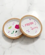 Δύο χειροποίητα σουβέρ Fresh Juice με σχέδιο ρόδι και lime, φωτογραφημένα πάνω σε λευκή μαρμάρινη επιφάνεια.