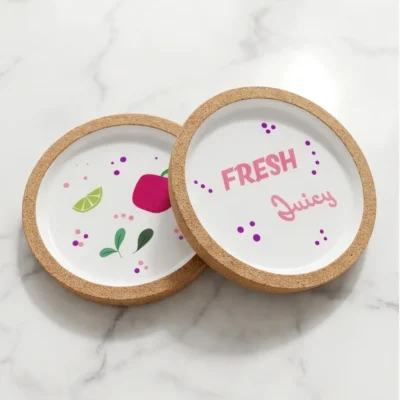 Δύο χειροποίητα σουβέρ Fresh Juice με σχέδιο ρόδι και lime, φωτογραφημένα πάνω σε λευκή μαρμάρινη επιφάνεια.