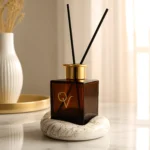 Luxury diffuser White Sandalwood σε γυάλινο Dark Amber μπουκάλι με χρυσό καπάκι πάνω σε λευκή βάση πορσελάνης Marble Gold