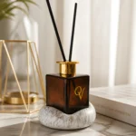 Κοντινό πλάνο diffuser Dark Amber με λογότυπο QV και βάση πορσελάνης Marble Gold